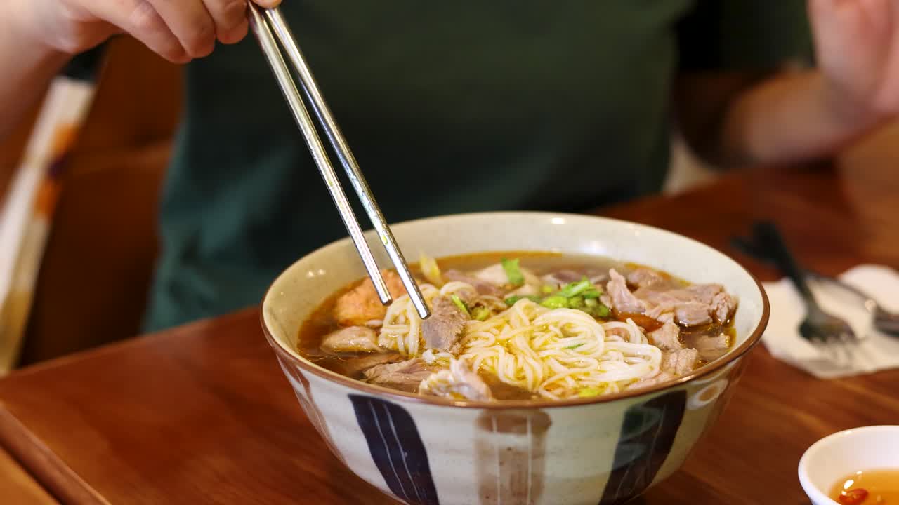 Primo piano di una persona che solleva carne da una ciotola di zuppa di noodle vietnamita