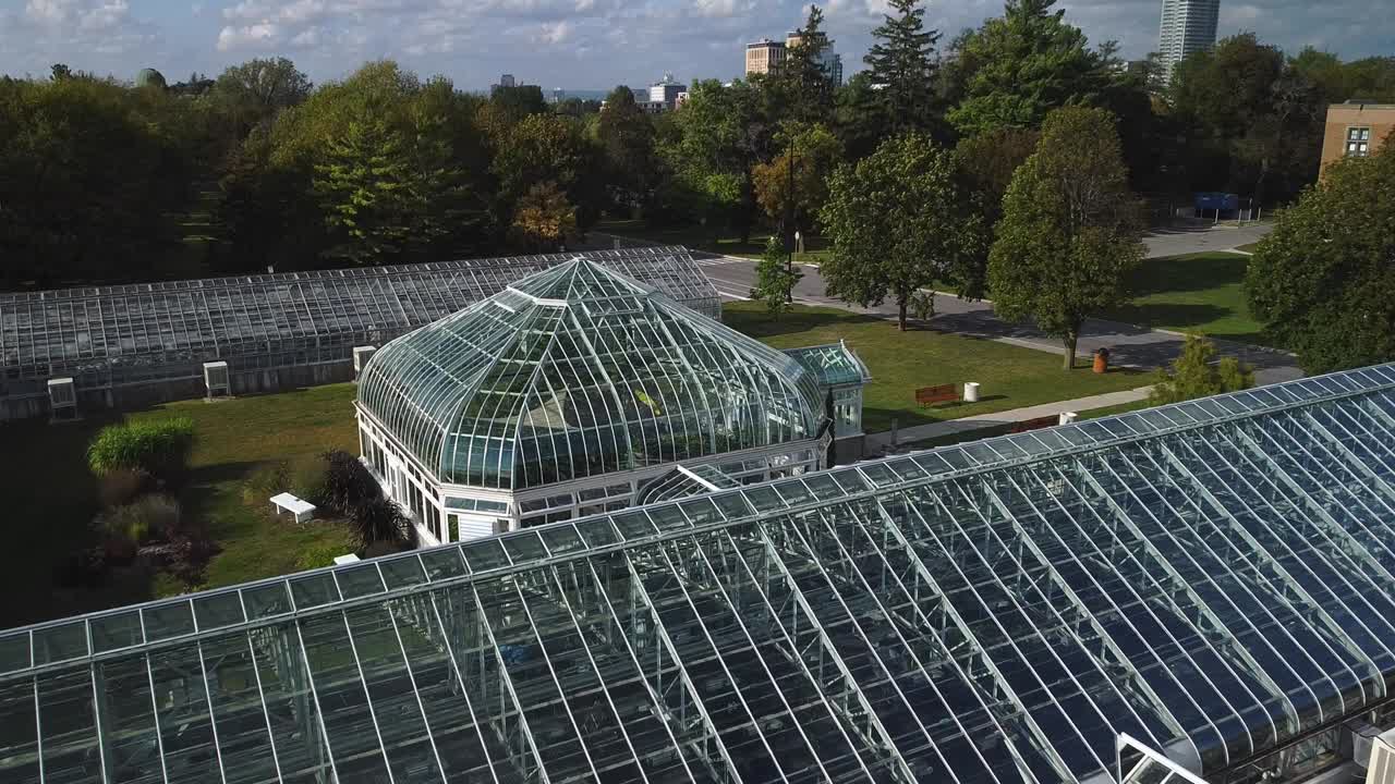 Flyover shot of ornate glass greenhouse with city skyline in background