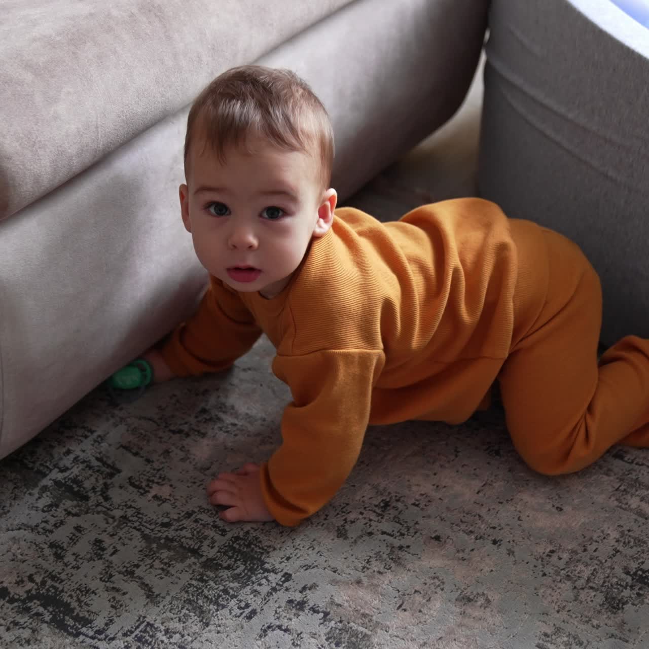 Toddler boy playing on the floor indoors. Adorable baby sitting by the soft basin with balls looking at his pacifier. Top view