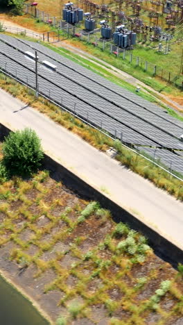 solar farm near the river. blue solar panels on the bank of the river in a sunny daytime. electric power station generate clean energy from the sun. aerial view. vertical video