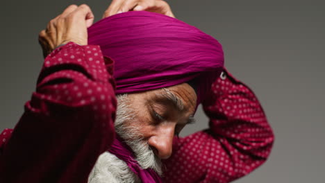 close up low key studio lighting shot of senior sikh man with beard tying fabric for turban against dark background 5