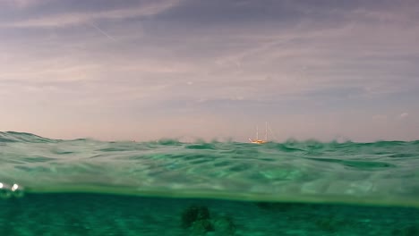 Vista-Medio-Bajo-El-Agua-Del-Velero-Amarrado-En-El-Horizonte-Y-Agua-De-Mar-Transparente-Con-Rocas-En-El-Fondo-Del-Mar