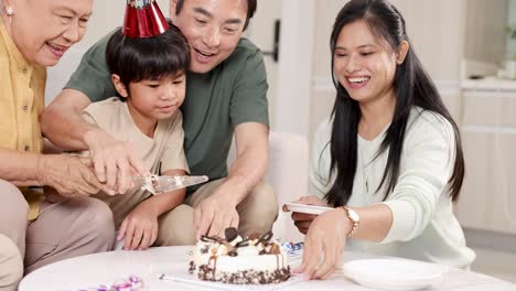 an asian family joyfully cuts a birthday cake together, surrounded by smiles and a festive atmosphere