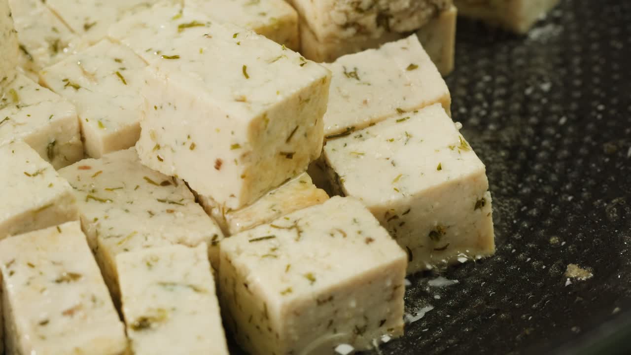 Fried tofu with sesame seeds and spices on cast iron pan, cooking japanese salad. Healthy ingredient for cooking vegan vegetarian diet food. Roasted tofu over black background.