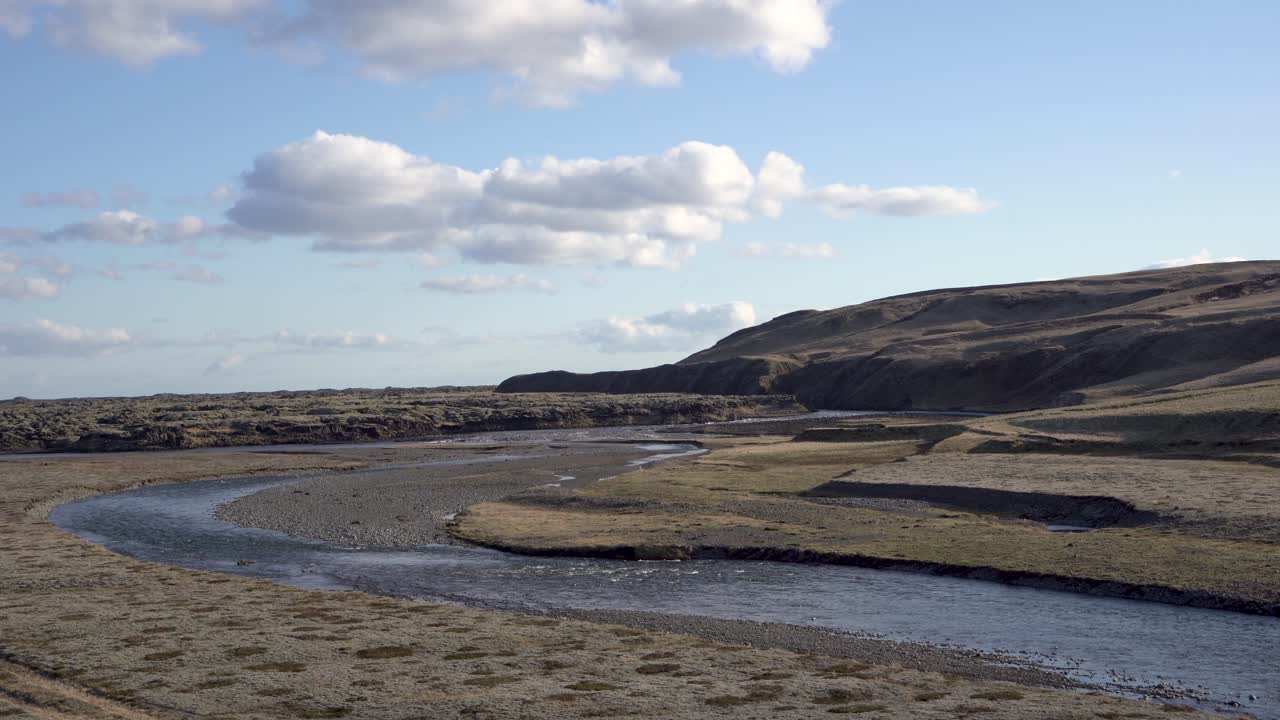 un río serpenteante que serpentea a través de un desértico paisaje islandés bajo un cielo azul con nubes dispersas