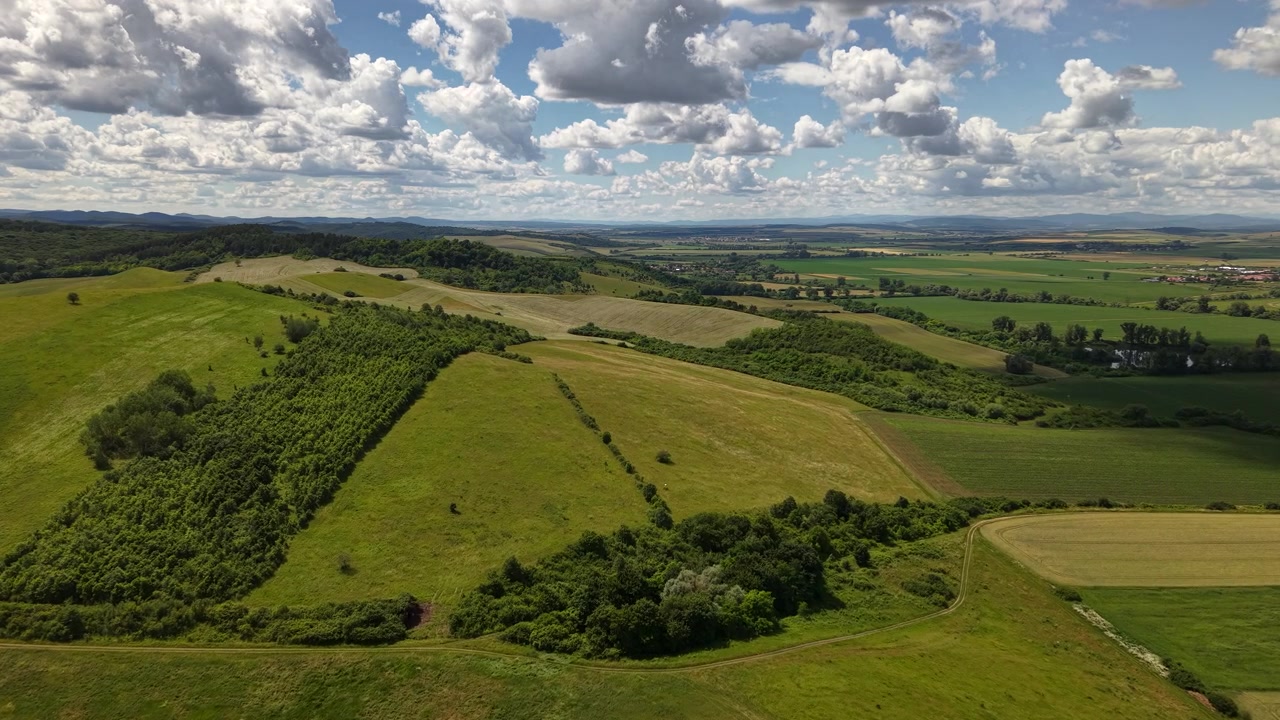 Una vista aérea panorámica de la vibrante y verde campiña húngara, con colinas ondulantes y campos agrícolas bajo un cielo dramático y nublado.
