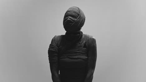 a mummy of a woman on a white backdrop slowly rises her head and look around