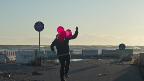 patinador cabalga hacia el mar sosteniendo un montón de globos rojos mientras algunos escapan en el viento
