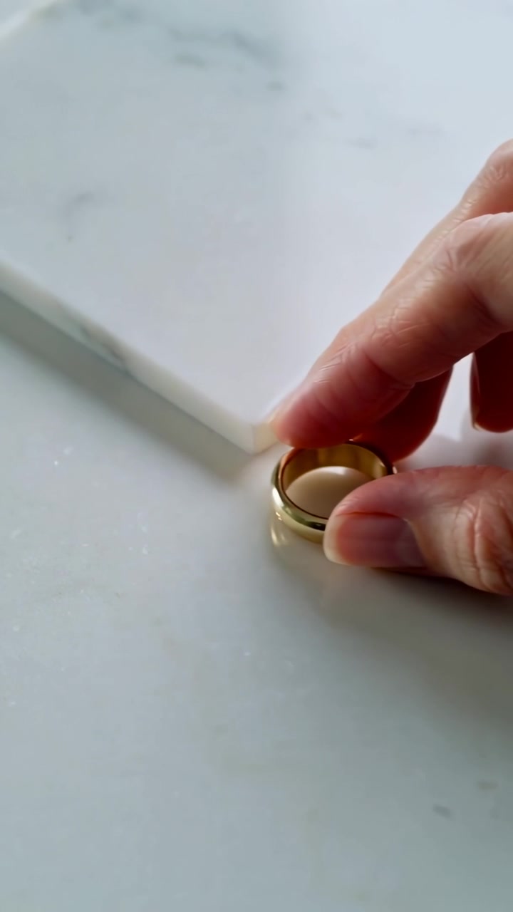 Video vertical: Una mano desnuda girando un anillo de oro sobre una losa de mármol, colocando el anillo junto a un azulejo.