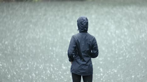 woman stands in the pouring rain against the background of a lake. shot on super slow motion camera 1000 fps.