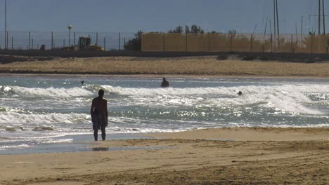 Tall-man-walking-on-beach-barefoot-in-summer,-waves-breaking-in-background