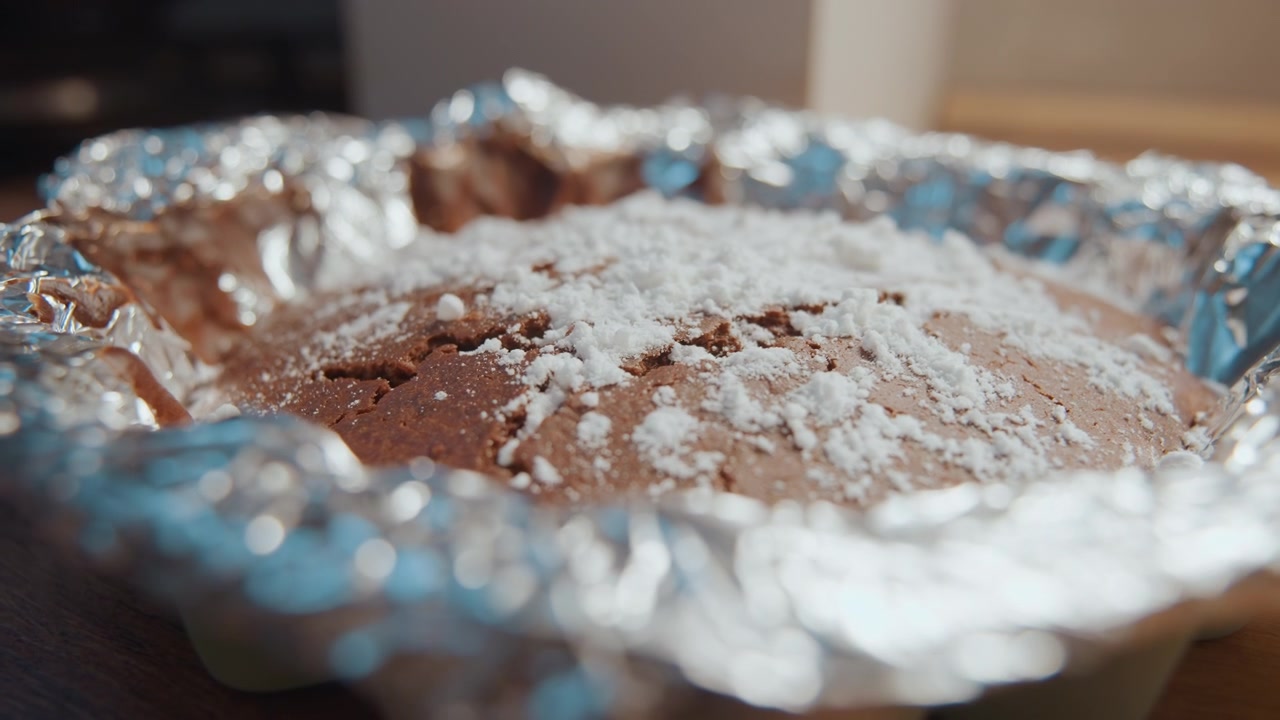 Escena de horneado de postres. Escena de cocina con pastel de chocolate recién horneado. Primer plano de pastel espolvoreado con azúcar en bandeja para hornear. Ambiente de cocina rústica mostrando a un panadero casero probando una receta de pastel de chocolate.