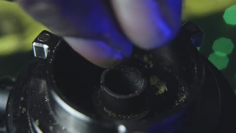 close up of a black mans hand as he slowly breaks up marijuana bud into the bowl of a vaporizer preparing to smoke the pot