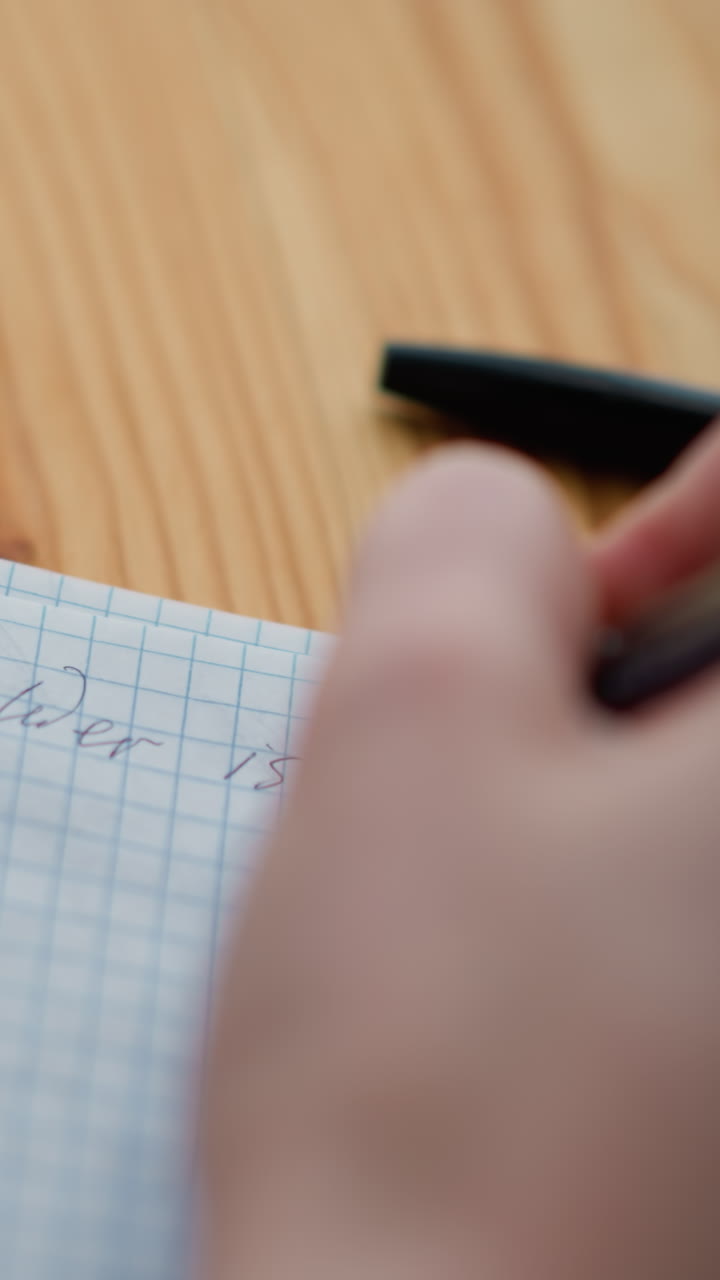 Close-up hand view of someone writing with pen, partially showing pen cover and tea cup on wooden table, conveying focus and contemplation while writing