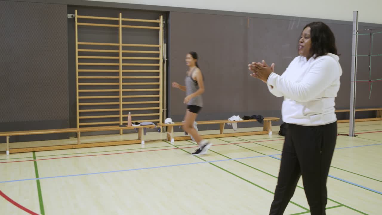 Mangfoldigt kvindehold og træner løber frem, kaster volleyball, samler sig til en øvelse i et fitnesscenter, plads til tekst.