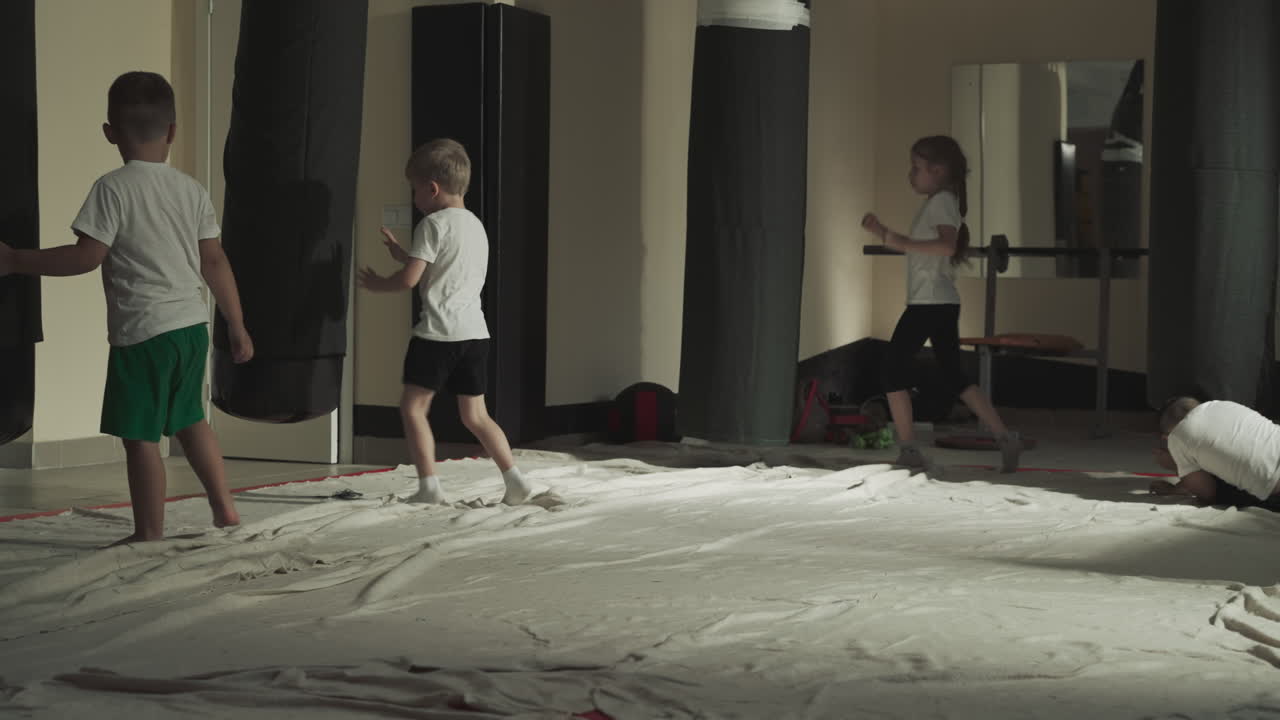 Kids kick punching bags in combat arts gym. Little sportsmen class trains actively at martial arts lesson in school slow motion. Junior fighters team