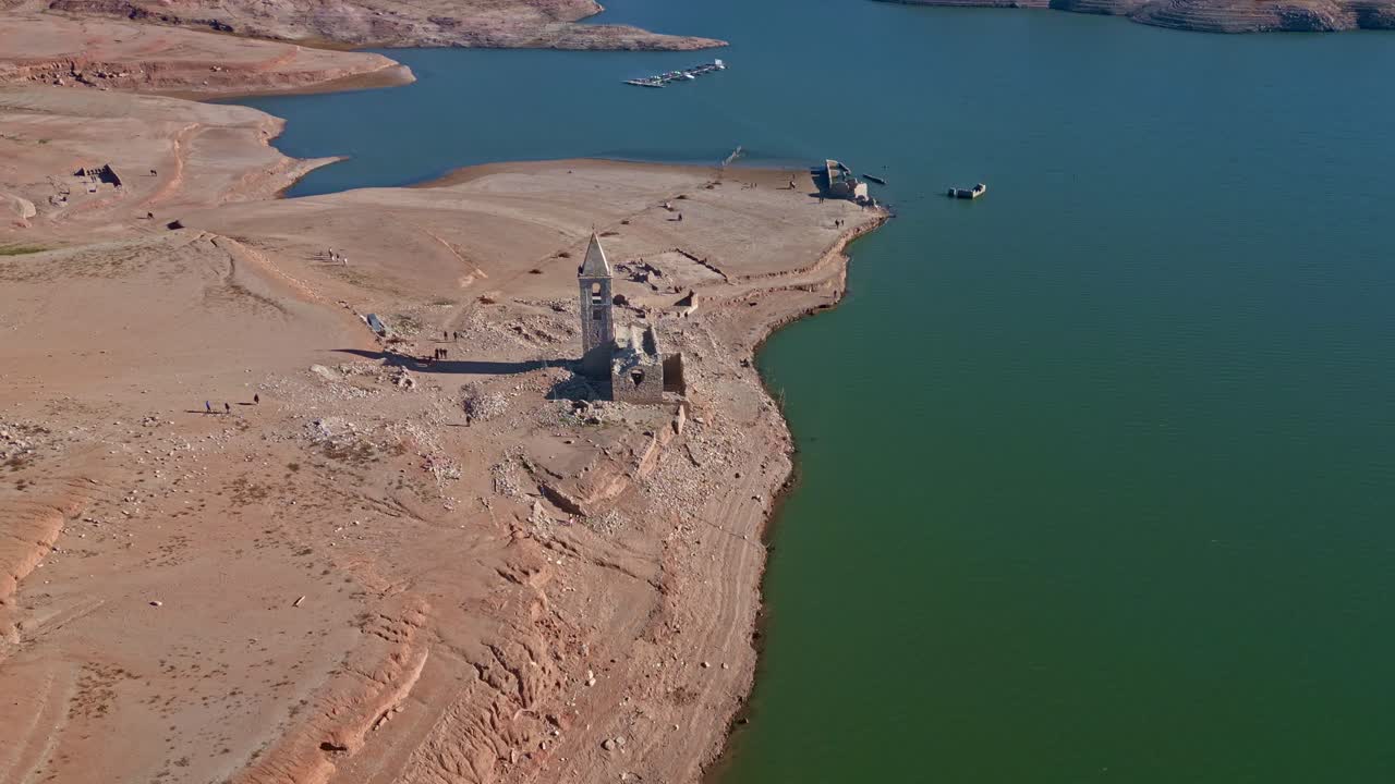 orbita sobre la iglesia en ruinas del embalse de sau, con agua muy baja y gente paseando por la orilla