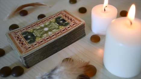 time lapse of a background with mystic cards deck near candles with flickering flames, stones and feathers