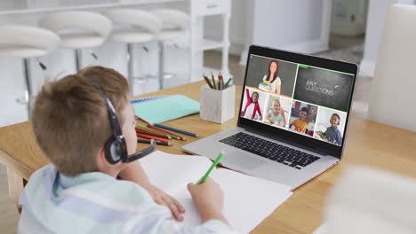 Schoolboy-using-laptop-for-online-lesson-at-home,-with-diverse-teacher-and-class-on-screen