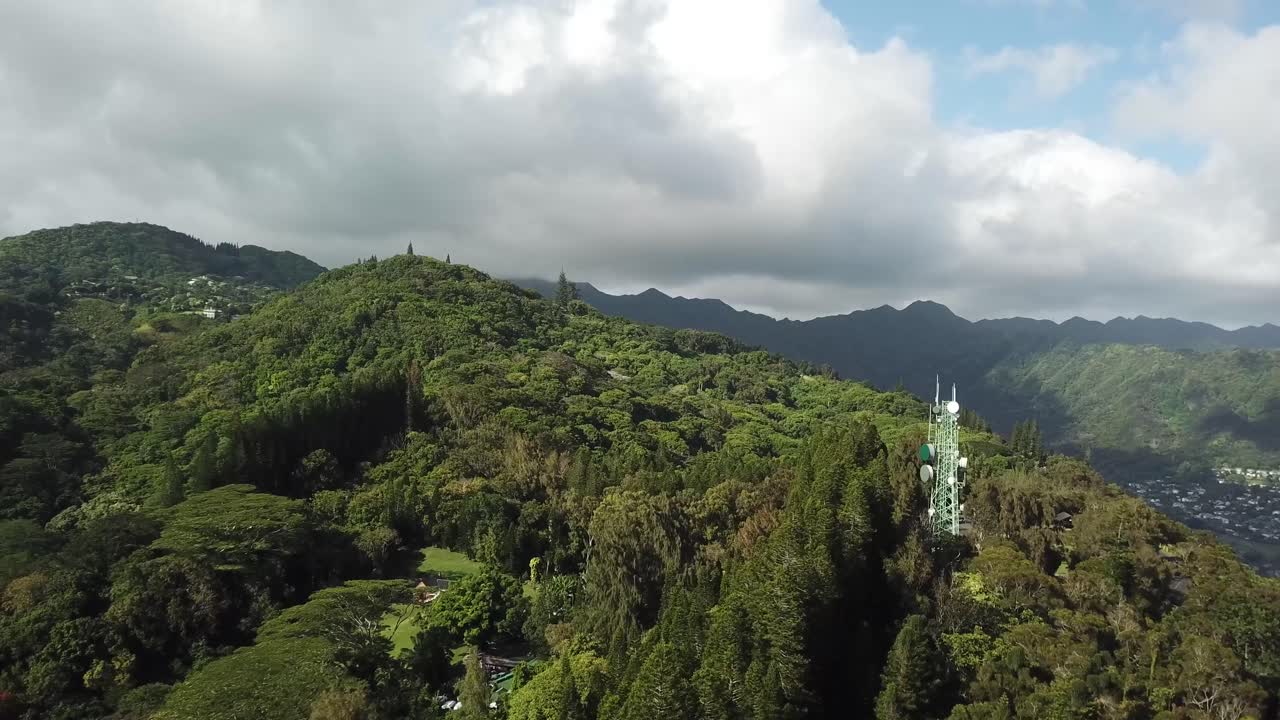 Transmission tower at dense growing Maliki valley trail surrounds by green mountains near Honolulu, Hawaii. Aerial wide shot