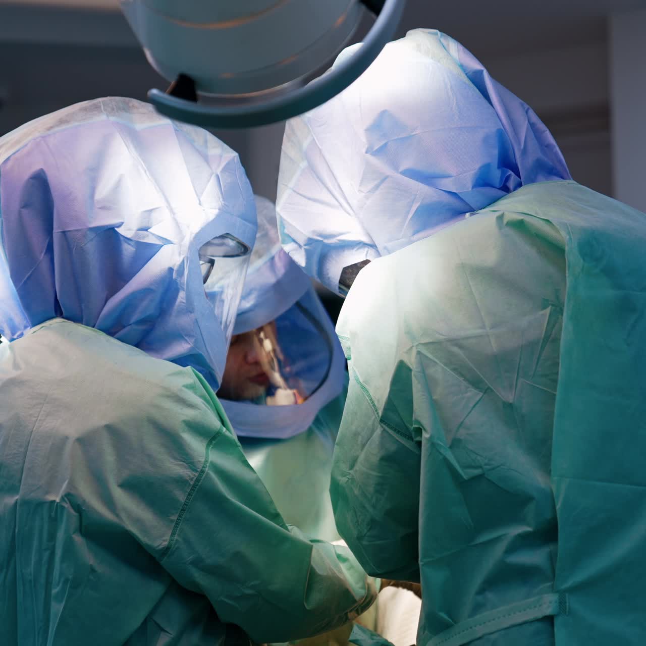 Rear view of three doctors surrounding the operational table at surgery. Doctors perform trauma procedure cooperating together