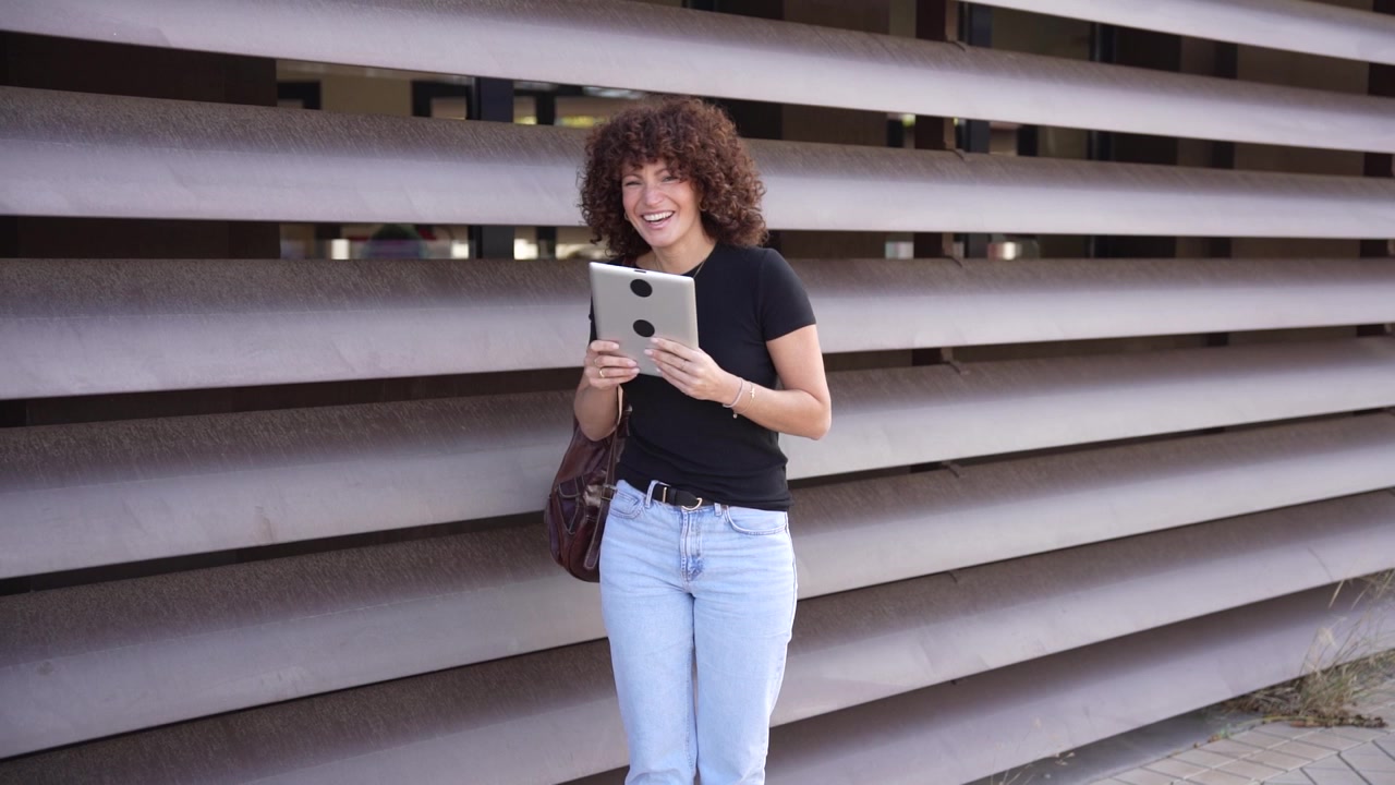 Una giovane donna si gode con gioia la tecnologia moderna, seduta all'aperto con il suo tablet in mano.