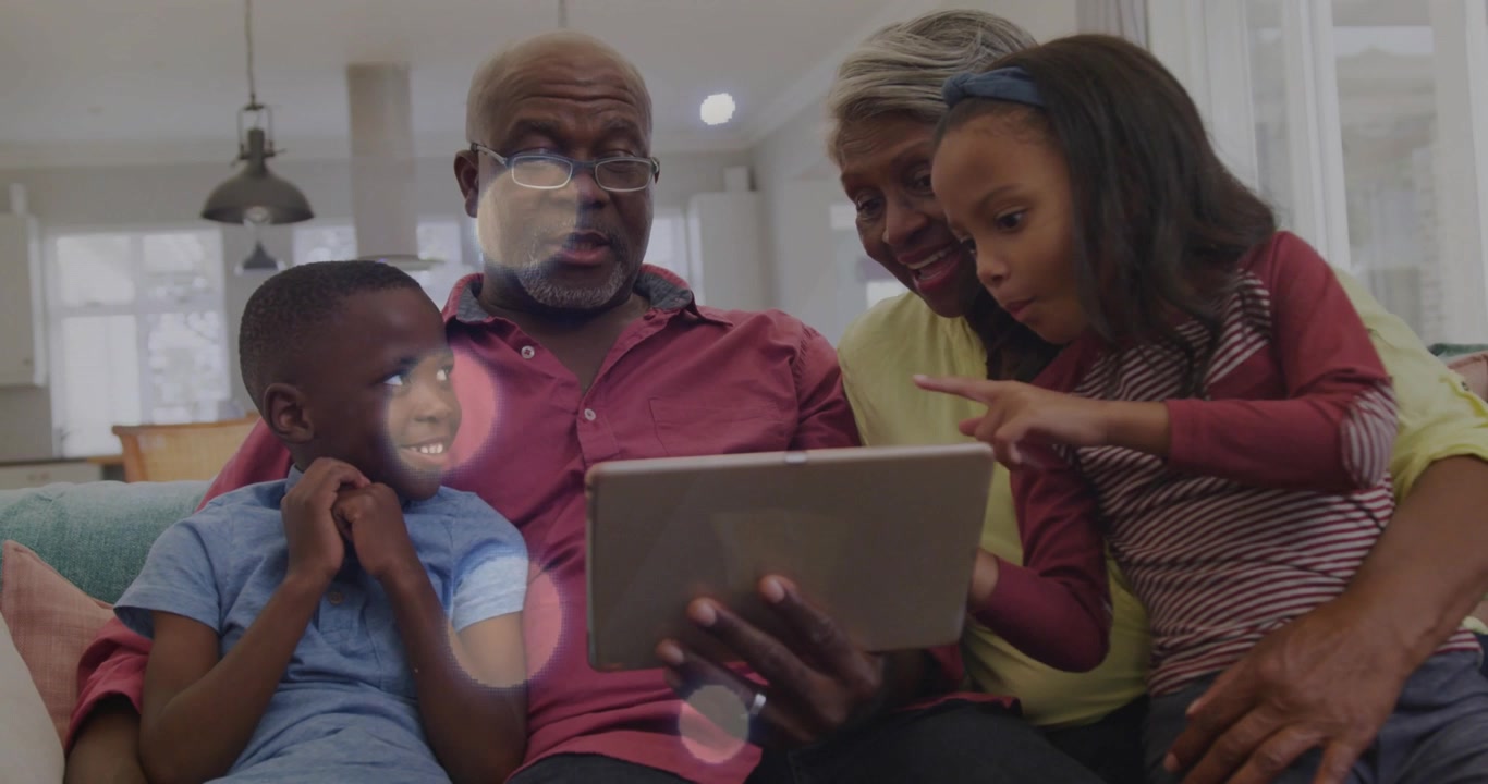 Girl reaching and tapping tablet, seniors leaning and smiling, family exploring tech with bokeh