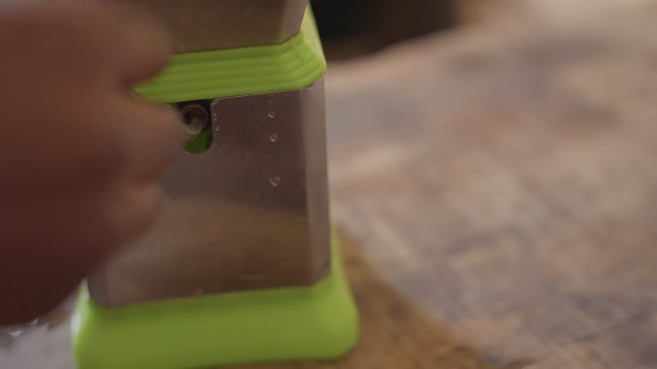 Primo piano di mani di bambino nero che girano la manovella di un piccolo trapano a mano su un banco da lavoro usurato, pratica di falegnameria per principianti concentrata, luce naturale calda, venature del legno e trucioli di metallo visibili, momento di apprendimento tattile
