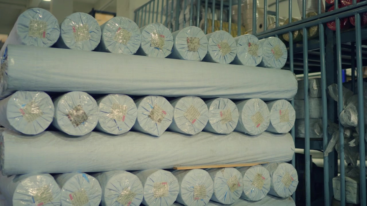 Rotoli impilati di tessuto di tela imballato, immagazzinati in un deposito di produzione di tende in Pakistan.