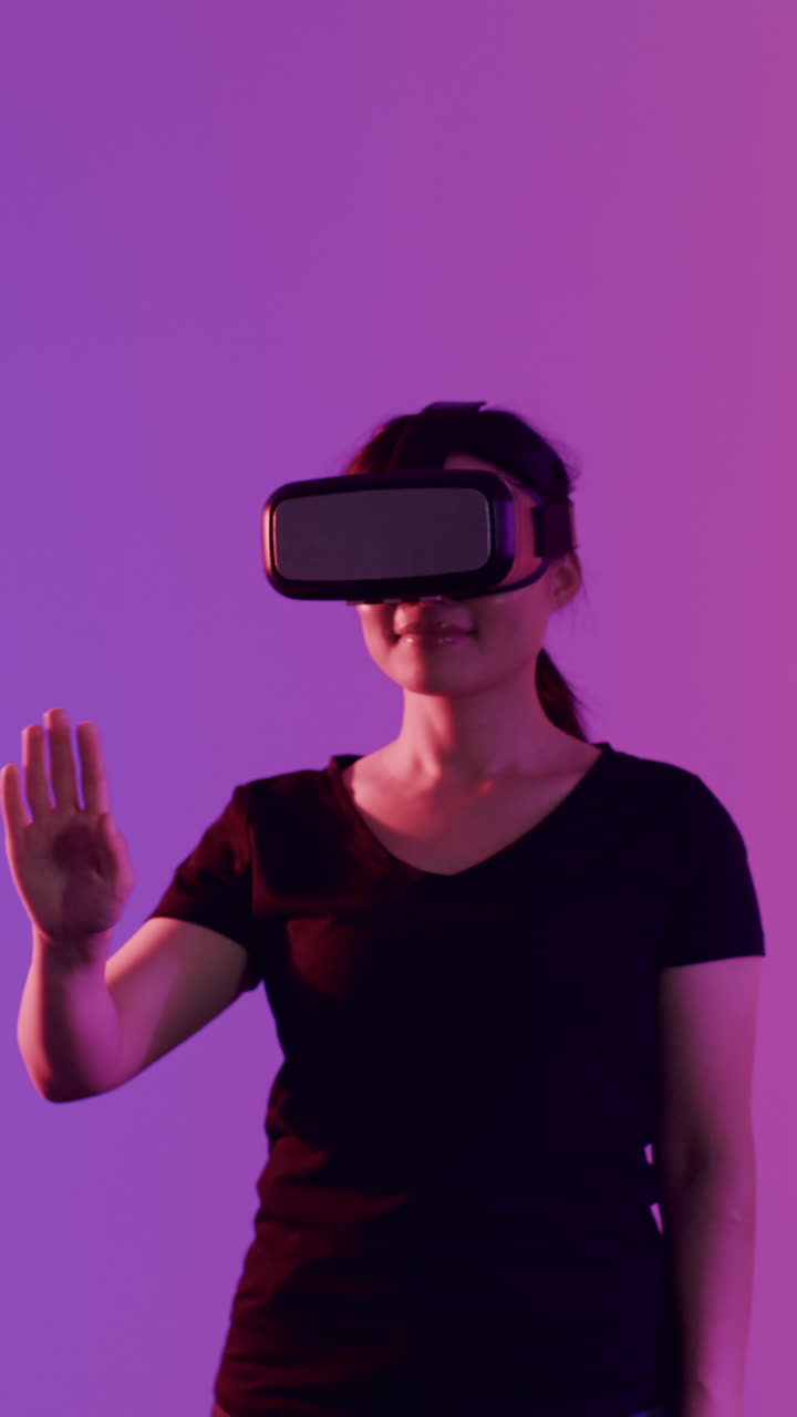 Vertical video of asian woman and woman using vr headsets on purple background, slow motion