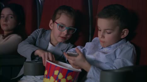 children eating popcorn in cinema. kids using mobile phone at cinema