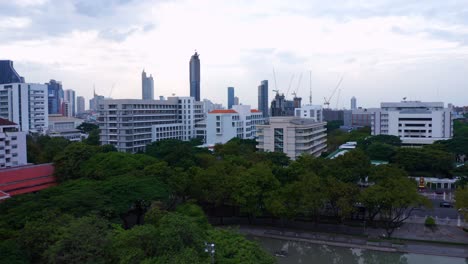 Elevándose-Por-Encima-De-La-Universidad-De-Chulalongkorn-Y-Revelando-Los-Rascacielos-Del-Centro-De-Bangkok-Con-El-Sitio-De-Construcción-De-La-Torre-Samyan-Visible---Bangkok,-Tailandia