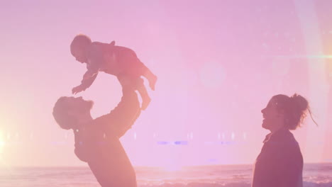 animation of light spots over happy caucasian couple with baby at beach