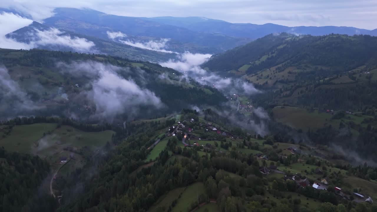 Aerial drone view of Mătișești village surrounded by drifting evening fog and layered hills of the Apuseni Mountains in Romania, showcasing a peaceful rural landscape after rain