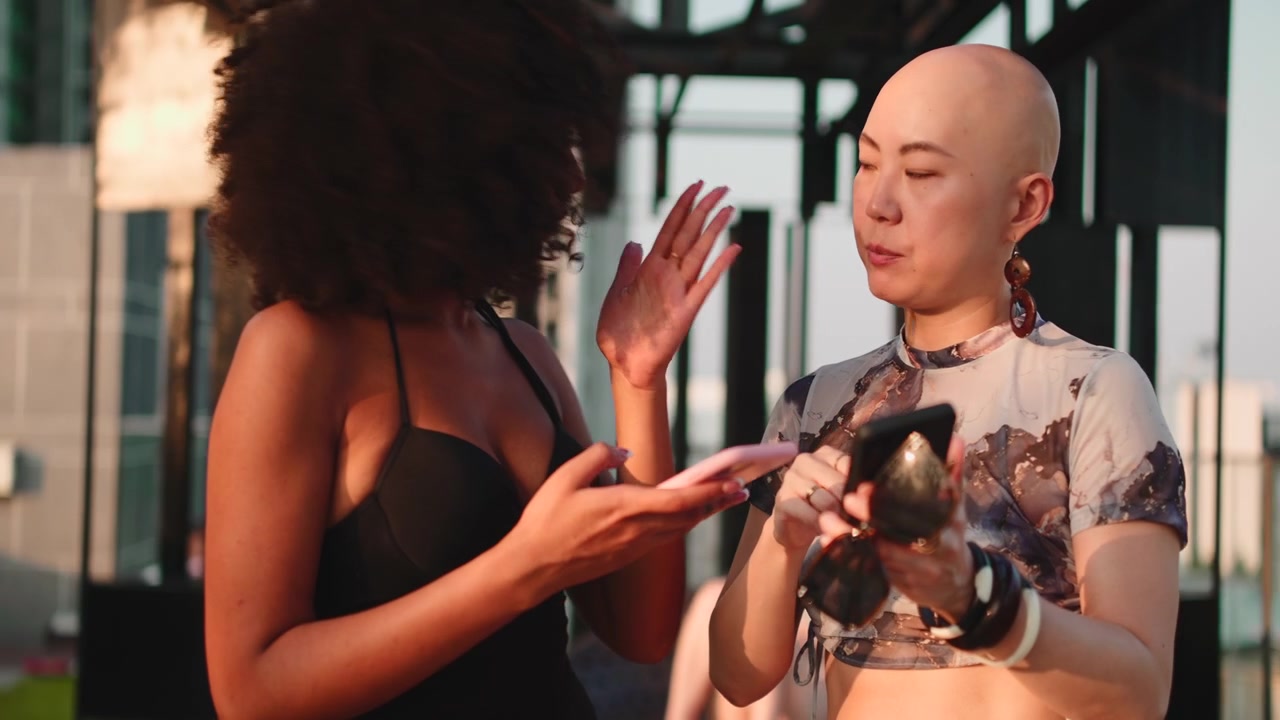 Two Young Women Talking and Using Smartphones on a Rooftop