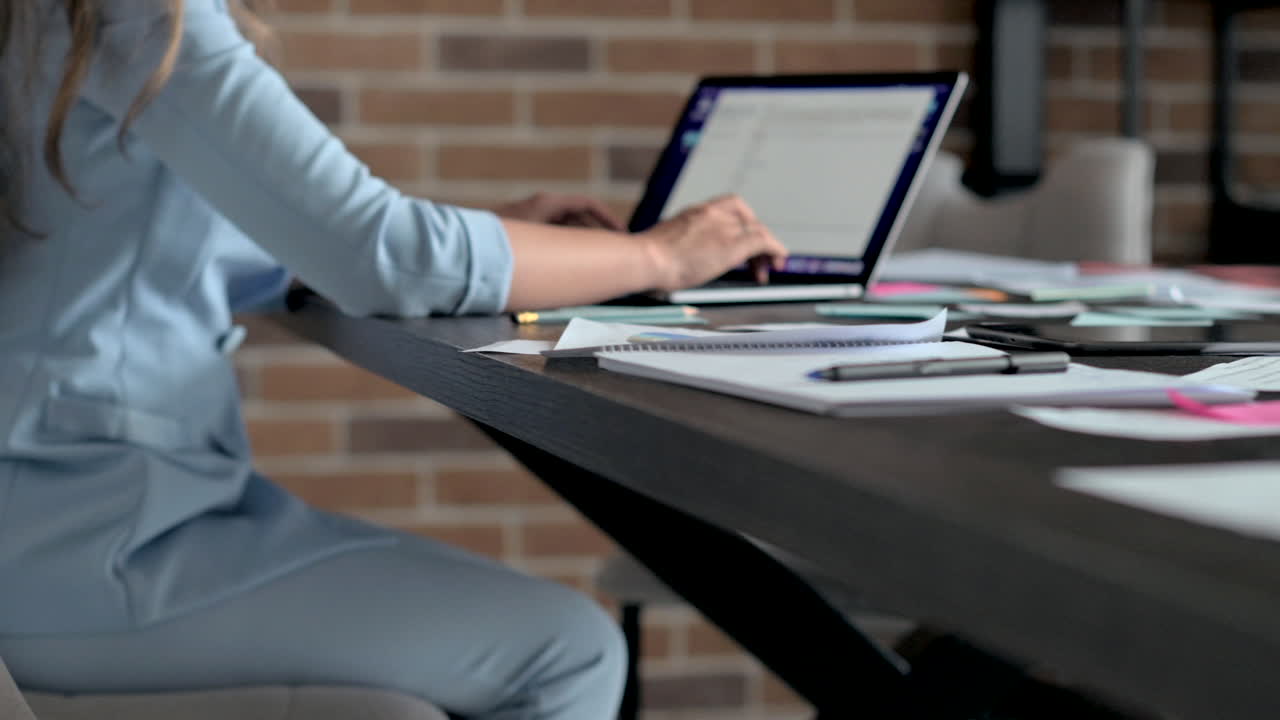 Donna con blazer blu che digita su un laptop a una scrivania in un ufficio