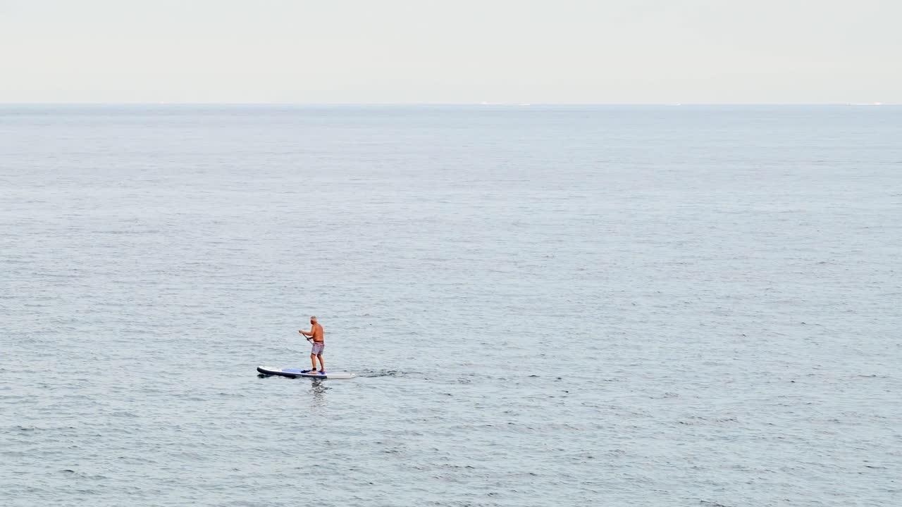 View of an old man swimming on a board near Mediterranean sea coast in Menton, France