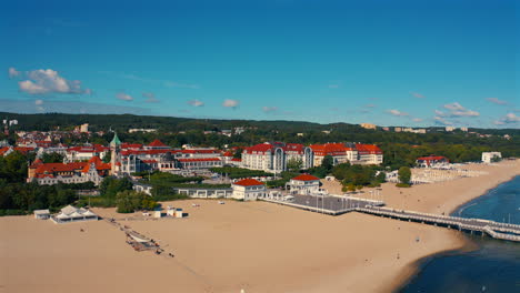 Aerial-view-of-drone-flying-towards-the-city-of-Sopot,-Poland-with-baltic-sea-and-pier-in-the-foreground-at-the-sunny-summer-day