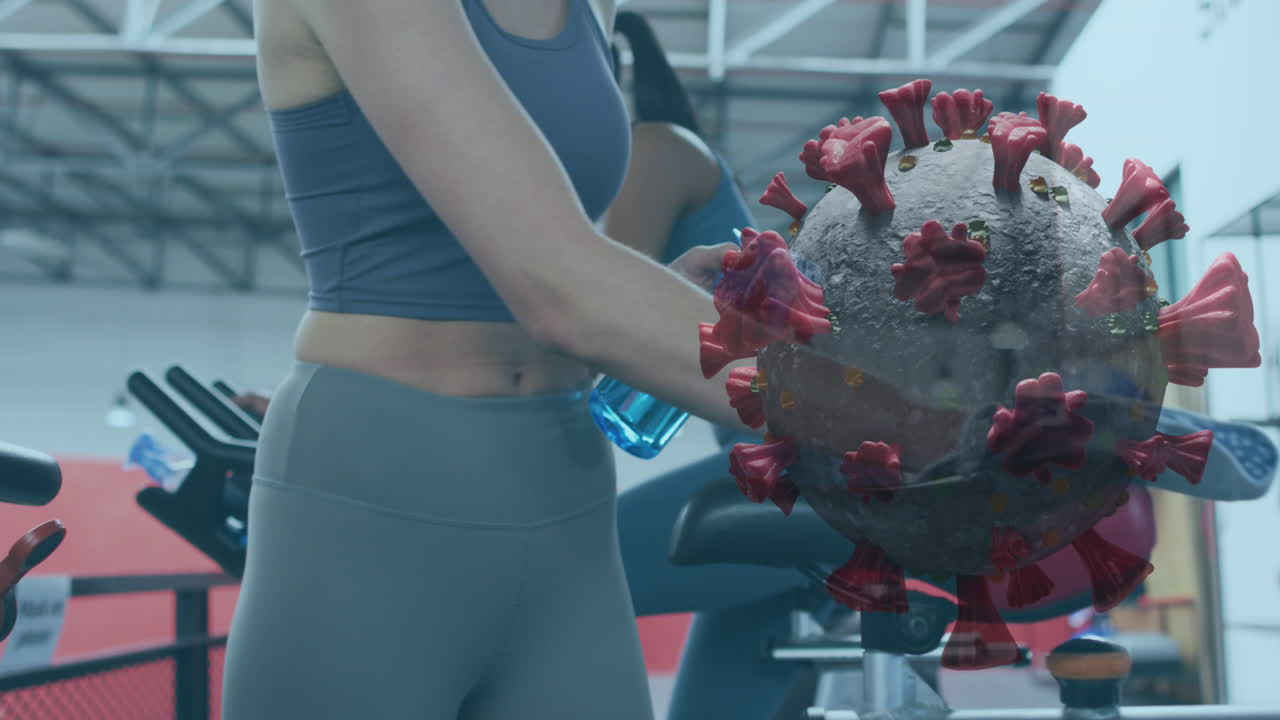 코로나 19 세포가 정지된 자전거에 소독제를 뿌리는 여성의 중간 부분에 떠다니고 있습니다.