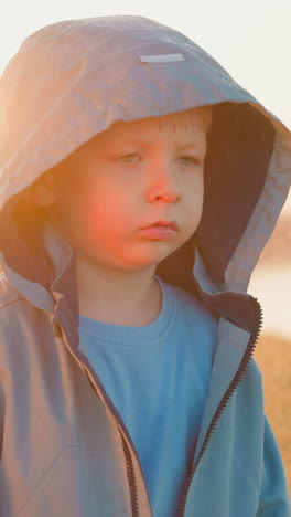 offended toddler child under rain on riverbank. scared little boy runs away from home surviving abuse on rainy day. abandoned kid in hood at stormy weather