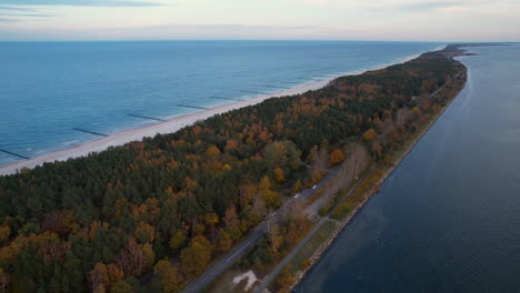 aerial view of a narrow strip of land with road, forest, and sea on both sides at dusk