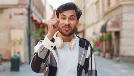 young indian man smiling excitedly and pointing to you choosing lucky happy winner in city street