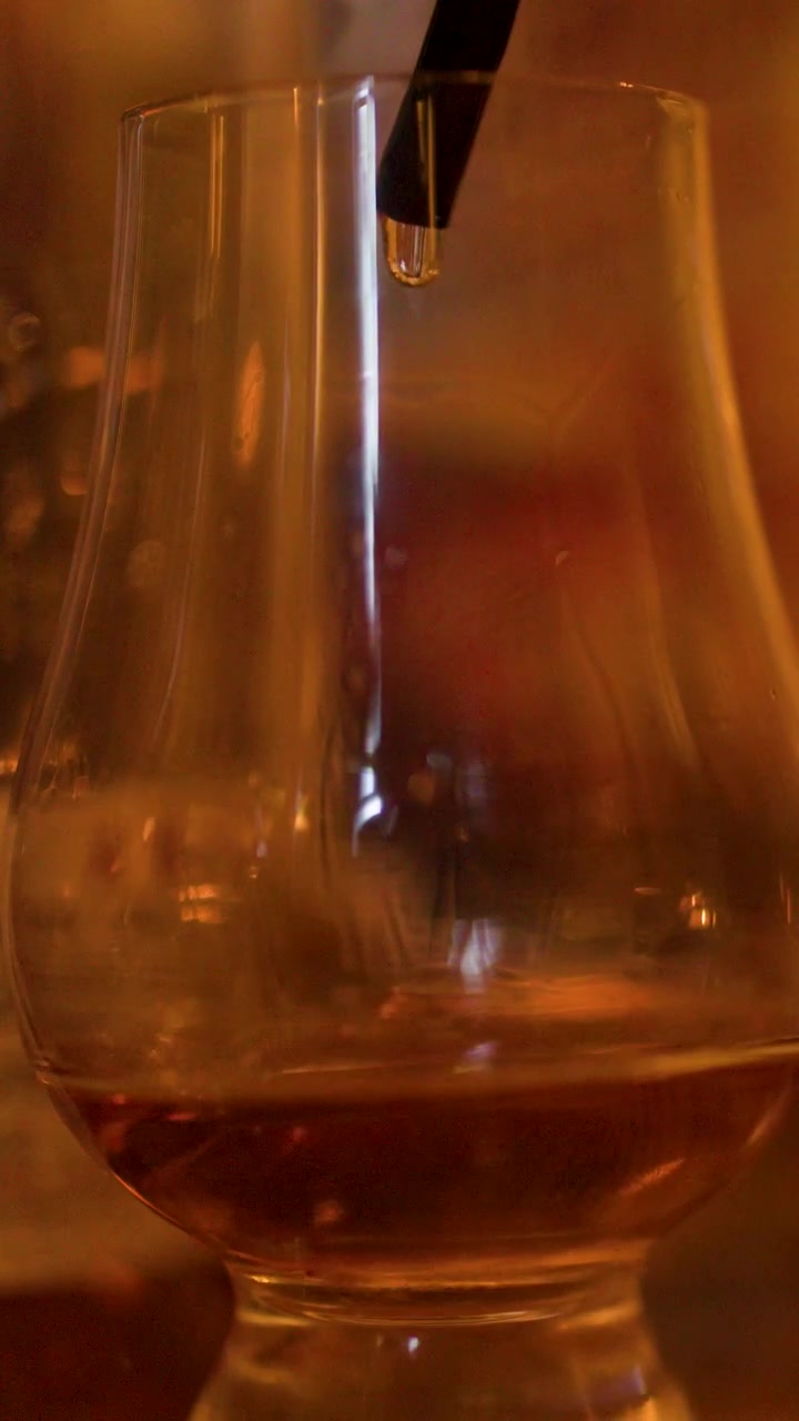Primo piano di un contagocce che aggiunge acqua a un bicchiere di whisky, bevanda ambrata, illuminazione serale calda