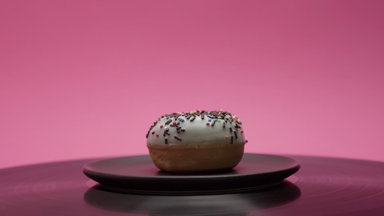 Delicious donut is turning on a black tray on a pink background