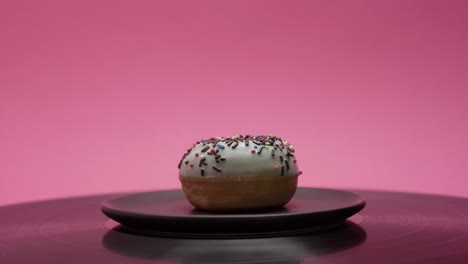 delicious donut is turning on a black tray on a pink background
