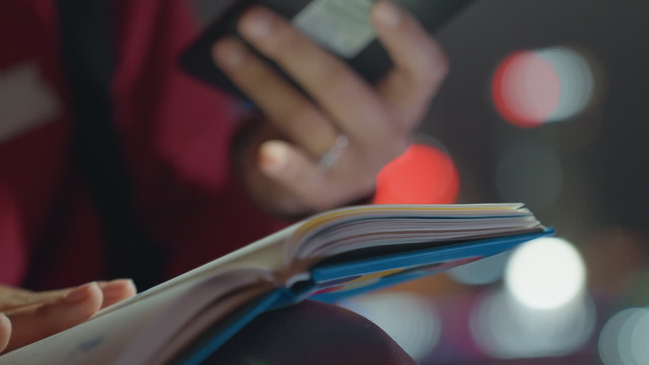 Studente notturno che legge un quaderno con il telefono accanto, mani che sfogliano pagine colorate, con le luci soffuse bokeh della città sullo sfondo. Un tenue bagliore dello schermo illumina gli appunti, un anello al dito, in un momento di studio intimo e concentrato.