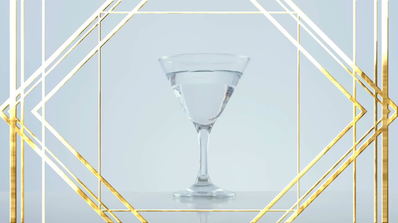 Motivo di design con cornice dorata su olive che cadono in un bicchiere da cocktail su sfondo grigio