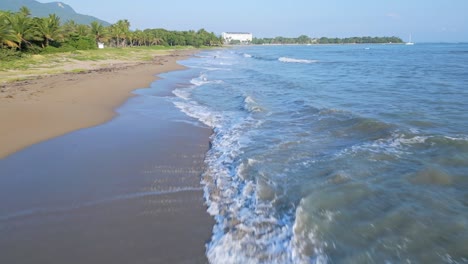 Low-altitude-flight-over-Playa-Dorada-with-reaching-waves-of-Caribbean-Sea-during-sunny-day