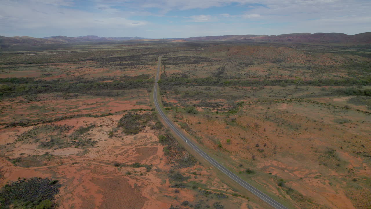 Alice Springs, Kuzey Bölgesi yakınlarındaki Batı MacDonnell Sıradağları'nda boş bir yolda giden bir minibüsün havadan drone çekim görüntüsü. Manzaralı çöl manzaraları ve engebeli dağlar