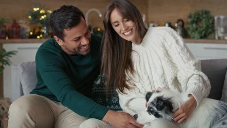 Happy-multi-ethnicity-couple-playing-with-dog-while-sitting-at-sofa-in-Christmas.